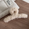Détail macro d'une pince à cheveux en peluche beige douce sur un support en bois - Laine d Agneau Douce / Abricot Beige