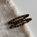 Détail de deux pinces à cheveux écaillées évidées sur un fond de tissu beige texturé - Tortoise