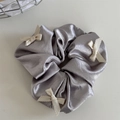 Detalle de coletero de satén gris plata con lazos crema sobre fondo liso neutro - Gris