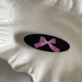 Dettaglio del fermaglio ovale nero con fiocco rosa su un piatto bianco a forma di conchiglia - Fiocco