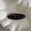 Detail of oval black hair clip with pink heart pattern on a shell ceramic tray - Heart