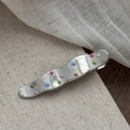 Vista macro de clip de pelo plateado con puntos de colores en tela beige - Forma de Onda con Puntos de Colores