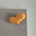 Nahaufnahme einer leuchtend orangefarbenen Herz-Haarklammer auf grauem Stoffhintergrund - Gelbe Herz Haarklammer