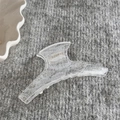 Détail montrant la texture en dentelle d'une pince à cheveux blanche translucide sur tissu gris - Pince en Arc (FJ891759) / Blanc