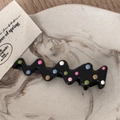 Macro view of black wave-shaped hair clips with colorful polka dots on a marble tray - Black Drip Oil - Radio Wave