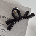 Detalle de pinza para el cabello con lazo negro brillante sobre fondo de lino rústico - Nudo Cruzado de Gelatina - Negro