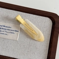 Detail of cream marble resin hair clip on a textured linen display tray - Yellow