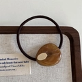 Detail of amber texture resin hair tie with a gold oval metal inlay on wooden tray - Brown