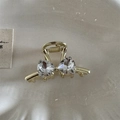 Detalle de una pinza para el cabello dorada con lazo y dos brillantes strass de corazón - Dorado