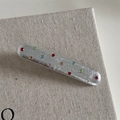 Dettaglio di un fermaglio y2k in metallo argento con strass colorati su sfondo materico - Forcina Argentata