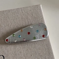 Vista macro di un fermaglio per capelli Y2K argento con strass colorati su lino grigio - Clip Goccia d'Acqua Argento