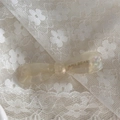 Détail d'une barrette à cheveux translucide avec logo doré sur de la dentelle blanche - Blanc