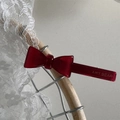 Dettaglio di un fermaglio a fiocco in acetato rosso con logo dorato su pizzo bianco - Rosso