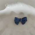 Detail view of denim texture acetate bow hair clip resting on a textured cream tray - Acetate Denim Texture - Ribbon Bow