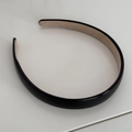 Dettaglio di un cerchietto in pelle nera con finitura lucida e fodera in velluto beige - Nero