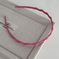 Detalle de diadema rosa ondulada con dientes antideslizantes sobre bandeja de lino gris - Rosa Roja