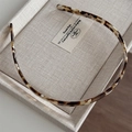 Close-up of tortoise shell acetate headband with non-slip teeth on grey fabric tray - Milk Coffee