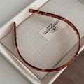 Close-up of tortoise shell headband with fine inner non-slip teeth on beige display tray - Amber Brown