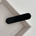Dettaglio di un fermaglio per capelli ovale nero lucido su un vassoio beige strutturato - Fermaglio a Barra Nero