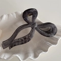 Close-up of a translucent smoky gray bow hair claw with silver glitter in a shell dish - Bowknot Style / Black