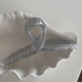 Detail von silberner Glitzer-Haarklammer mit schimmernder Harztextur auf Schalenteller - Kleiderbügel Modell / Silber
