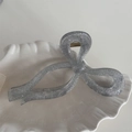 Close-up of a silver glitter bow-shaped hair claw clip on a white decorative shell plate - Bowknot Style / Silver