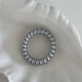 Primo piano di un elastico a spirale grigio argento su un vassoio di ceramica bianca - Stile Argento (FQ88495) / Argento
