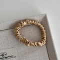 Detail of champagne gold silk scrunchie with soft satin texture in a linen tray - Yellow