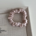 Detail of soft pink silk satin scrunchie with pleated texture on beige fabric tray - Light Pink