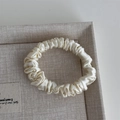 Detailed texture of ivory silk scrunchie with soft sheen on a textured display tray - Off-white