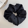 Gros plan d'un chouchou noir avec motifs de cœurs et texture de tissu doux sur fond blanc - Coeur Noir