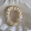 Macro shot of cream pleated scrunchie with a large pearlescent resin bead in a shell tray - Beige