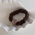 Close-up of brown pleated scrunchie with a translucent amber bead in a shell dish - Brown