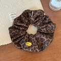 Détail d'un chouchou léopard avec pendentif en métal doré sur une surface en bois - Léopard Café