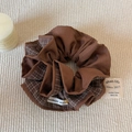 Detail eines braunen Karo-Scrunchies mit Handmade-Etikett auf einer gewebten Matte - Kaffee-Karo Haargummi