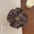 Detail eines dunkelbraunen Blumen-Haargummis mit Vintage-Baumwoll-Leinen-Textur auf Tisch - Woll-Scrunchie / Braun