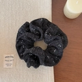 Nahaufnahme eines schwarzen Blumen-Scrunchies mit weißen Punkten auf gemütlichem Textur - Woll-Scrunchie / Grauschwarz