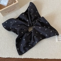 Close-up of black floral scrunchie with white daisy print on a textured beige mat - Grey Paisley Bandana