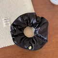 Detailed close-up of dark satin scrunchie with shiny texture and gold metal tag - Black
