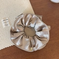 Gros plan détaillé d'un chouchou en satin champagne avec un pendentif logo doré poli - Champagne