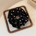 Nahaufnahme eines schwarz-weißen Polka-Dot-Haargummis auf einem Holztablett für Haarstyling - Schwarzer Polka Dot