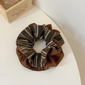 Makroaufnahme von braun gestreiften Oversize-Scrunchies auf weißem Tisch mit Holzdekor - Gelbkaffee