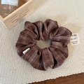 Dettaglio di un elastico per capelli a scacchi marroni su un tappeto di paglia - Marrone