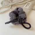 Détail d'un chouchou en peluche grise avec nœud décoratif sur fond de tissu beige doux - Nœud en Peluche Violet