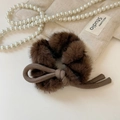 Détail d'un chouchou en fausse fourrure marron avec nœud sur fond beige élégant - Nœud en Peluche Café