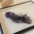 Close-up of plush bow hair clip with leather cord and gold embossed metal pendant - Purple