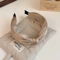 Close-up of elegant knotted satin headband in champagne gold on a linen cushion - Beige