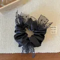 Détail d'un chouchou en satin noir avec nœud en tulle à pois sur un set de table tissé - Noir