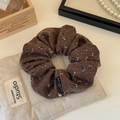 Detail van bruine gebreide haars scrunchie met bloemenprint, goudkleurige hanger en label - camel