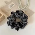 Dettaglio ravvicinato di un elastico per capelli a scacchi bianco e nero su lino beige - Quadri Nero